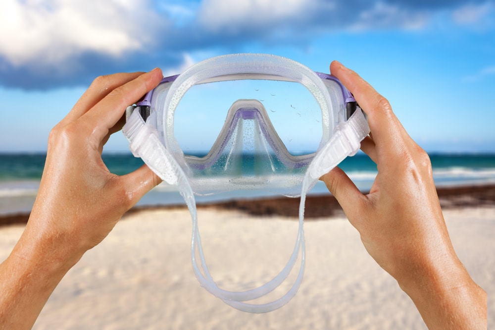 A man holds a snorkel mask in his hand against a clear blue sky background 