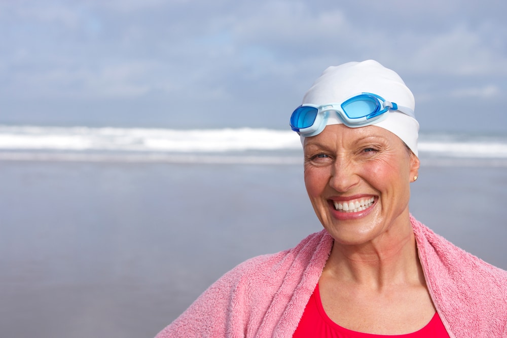 Senior woman in bathing suit. swimming cap  smiling at beach