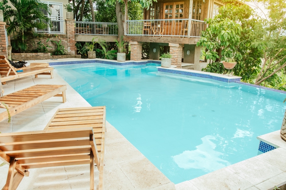 A Beautiful And Crystal Clear Swimming Pool Surrounded By Trees with Adirondack Chairs Around