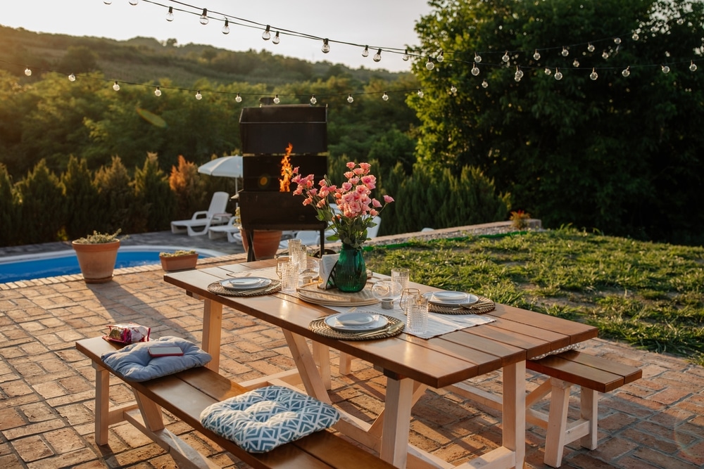 Nicely set diner table with different kinds of plates and glasses on it in the beautiful backyard 