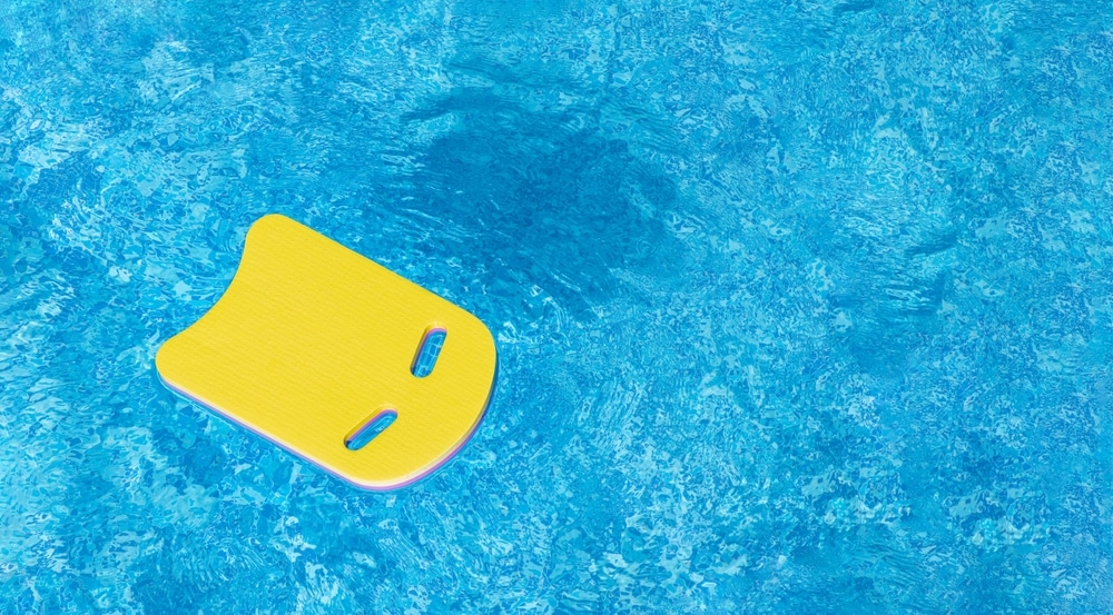 Yellow Swimming kickboard on blue water surface of swim pool.